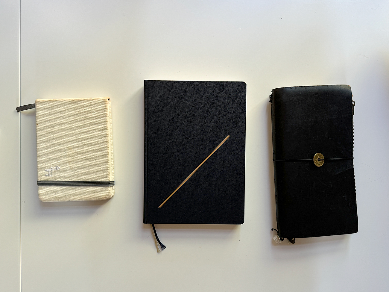 Three journals, side by side: an Etchr canvas sketchbook, a Hobonichi planner, and a black Traveler's Company standard-sized notebook.