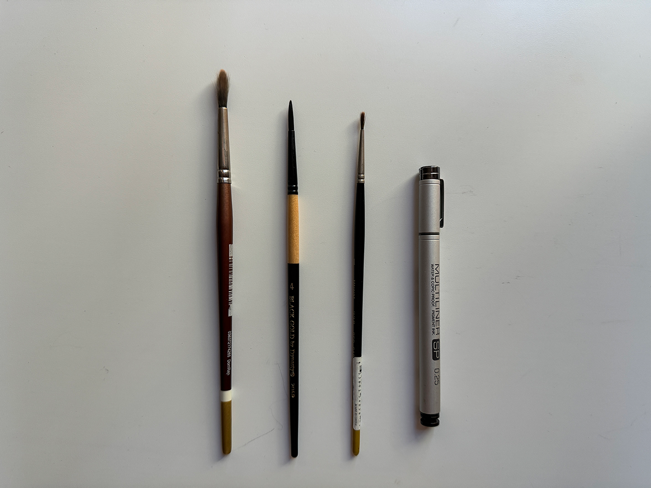 Four drawing implements, from left to right: Robert Simmons white sable round brush #6; BLACK GOLD by Dynasty liner brush #4; Utrecht red sable round brush #1; and my trusty Copic multiliner pen in 0.25.